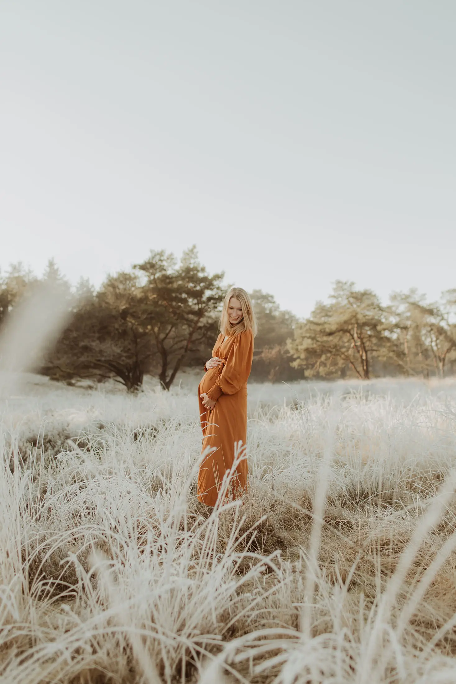 Zwangere vrouw wandelt door hoog gras in een oranje jurk