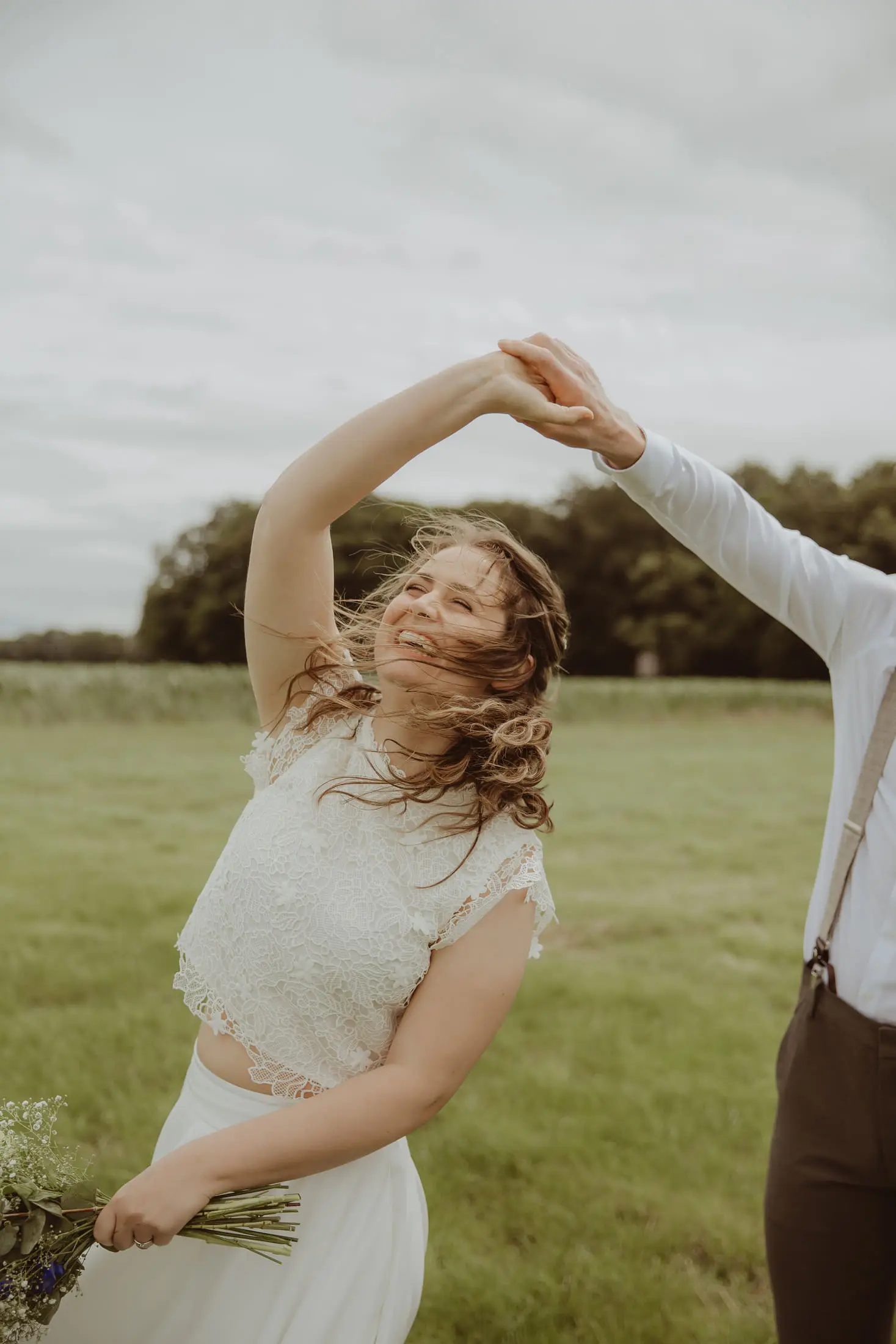 Bruid danst speels met haar jurk in een groen landschap